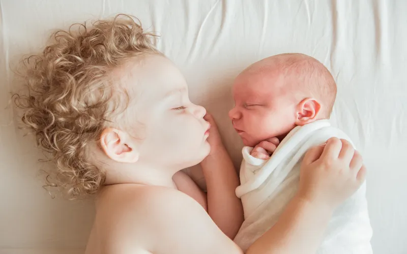 Newborn family poses showing an older sibling gently touching the baby's cheek