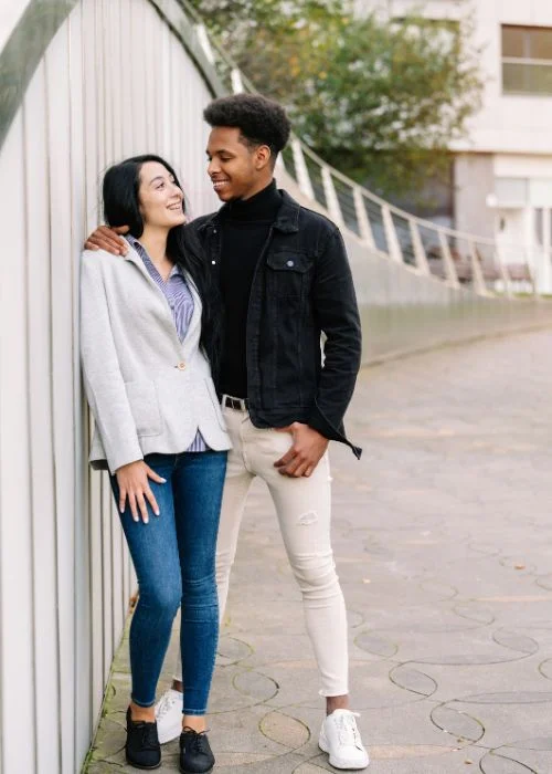 Couple standing close together on a sidewalk, woman resting her head on her partner's shoulder