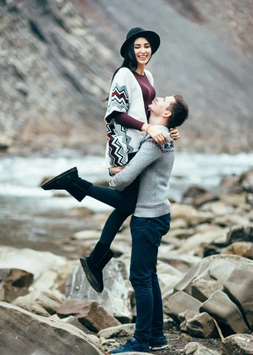 Man lifting his laughing partner off her feet on rocky riverbank terrain