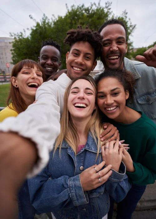 Diverse group of friends gathering closely together for a joyful outdoor group selfie filled with genuine smiles.