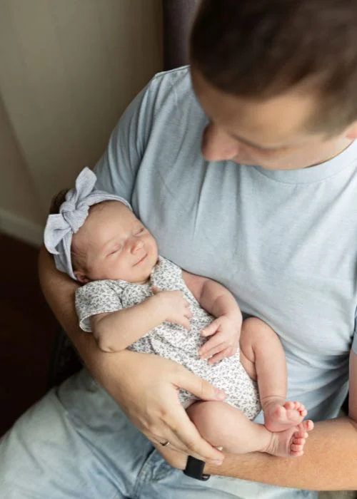 Parent gently holding a swaddled newborn against their chest in soft blue lighting