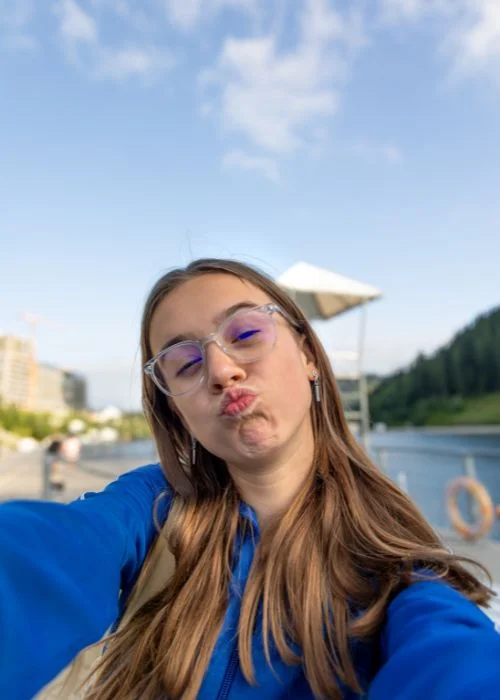 Woman making a playful pout while taking a selfie near a waterfront, featuring one of the most popular face poses for selfies.