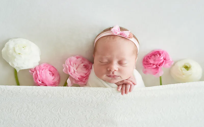 Sleeping newborn in a blush pink monochrome setup surrounded by pink peonies