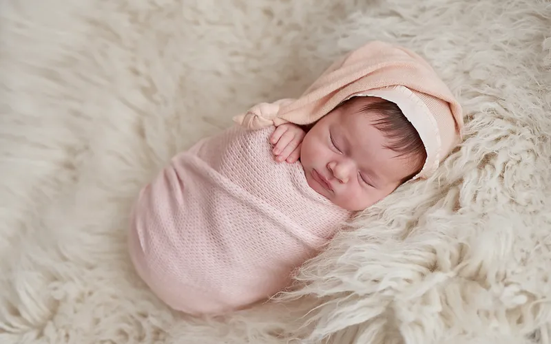 Newborn potato sack pose with baby curled in a knit wrap and matching hat