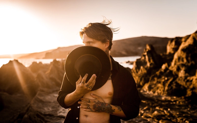 Man with dark hair holding hat outdoors