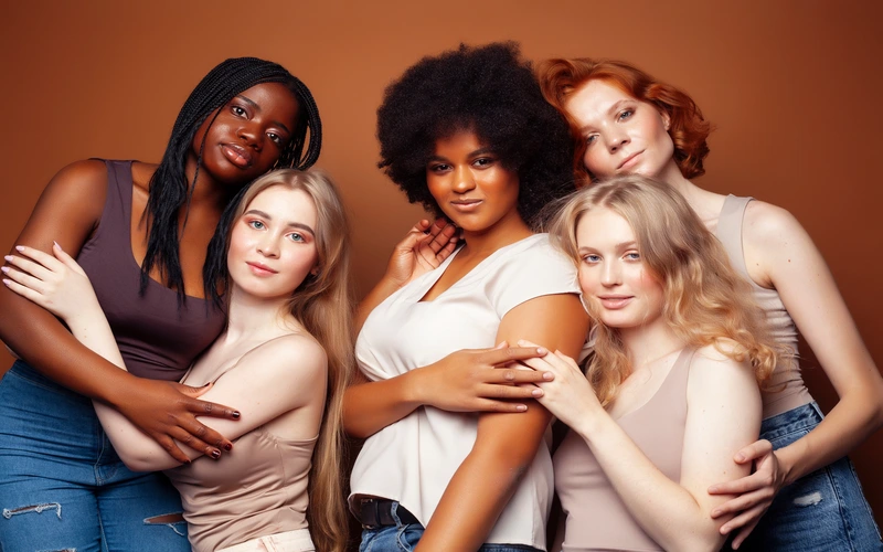 Five women with different skin tones and body shapes posing together against a warm background