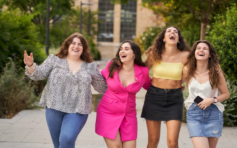 Four women laughing together outdoors, showing the joy behind a body confidence photoshoot