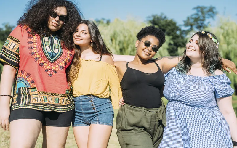 Four friends laughing outdoors with arms around each other, showing genuine expression in a body confidence photoshoot