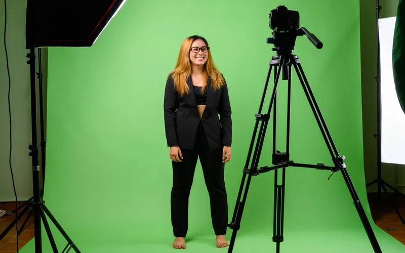 smiling woman posing in front of tripod and green screen