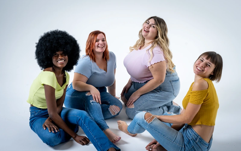 Four women of different sizes sitting together in denim, each posed in a way that feels natural to them