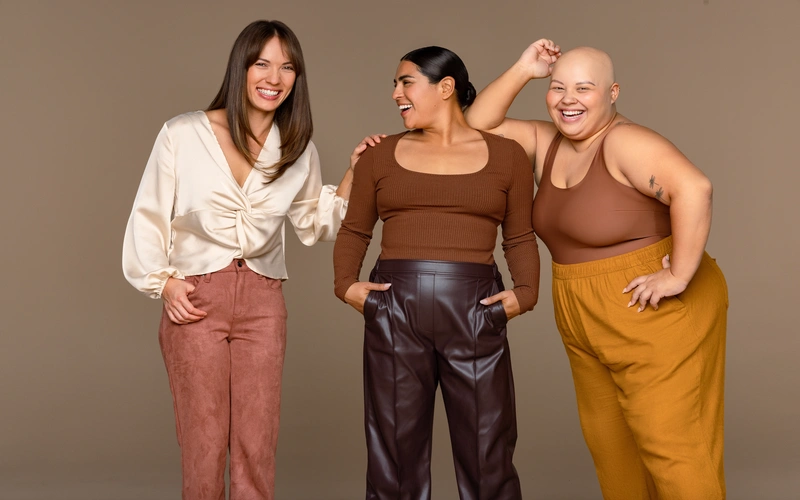 Three women of different body types laughing together during a body positivity photoshoot