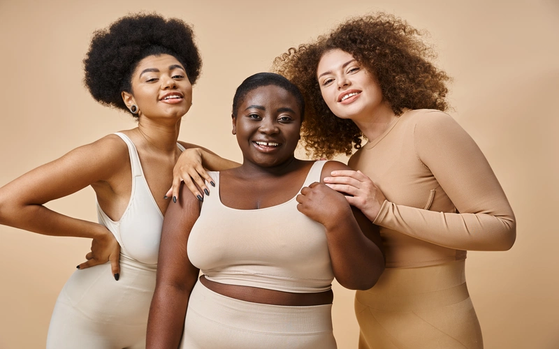 Three women in neutral-toned outfits posing close together without hiding their curves