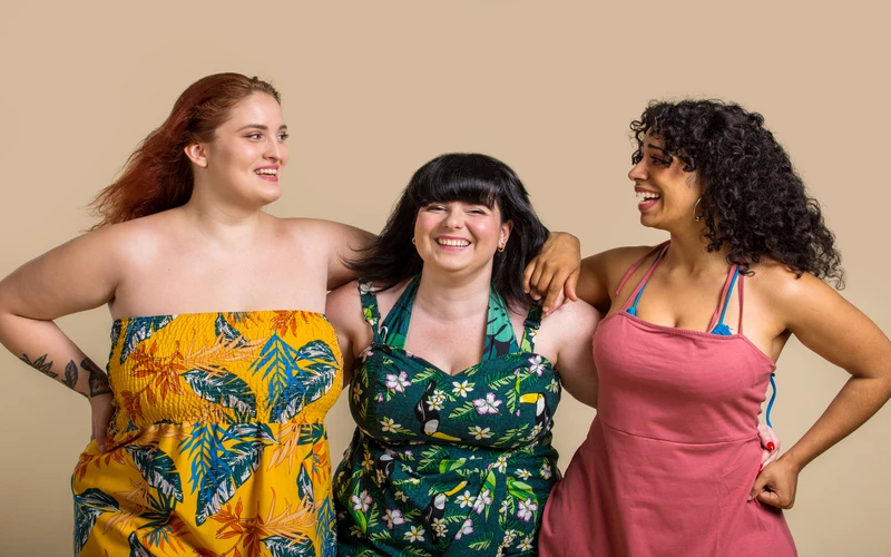 Three women in colorful patterned outfits posing together against a plain backdrop