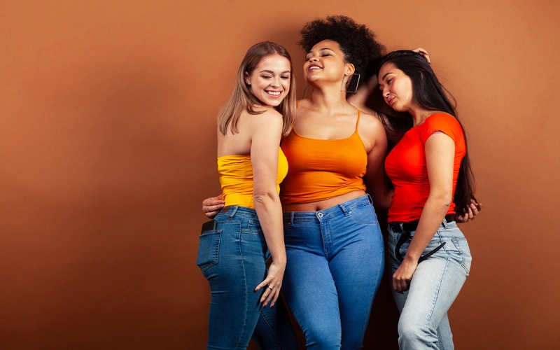 Three women in bright colors posing together with natural movement, a technique often used in body confidence photoshoots