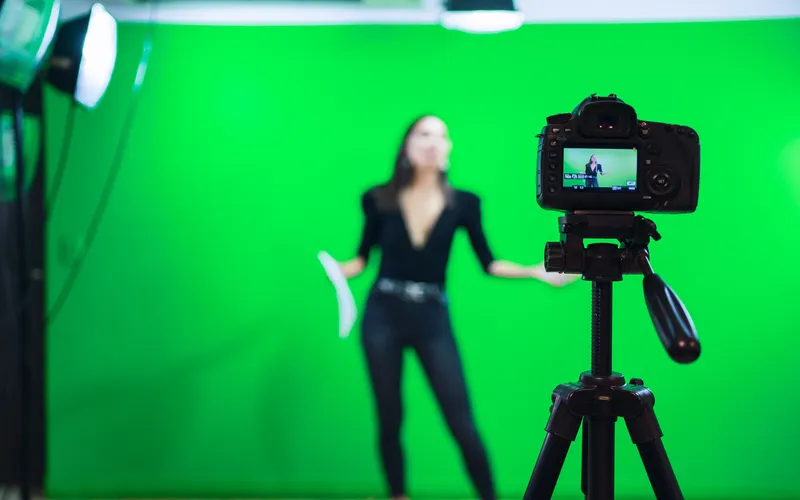 woman in black suit against a green screen and camera capturing it