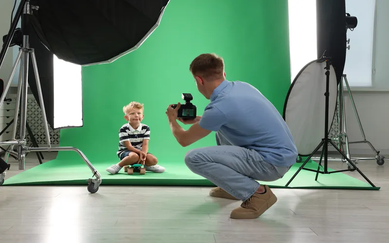 young boy posing for a photoshoot against a green screen while the cameraman clicks his picture