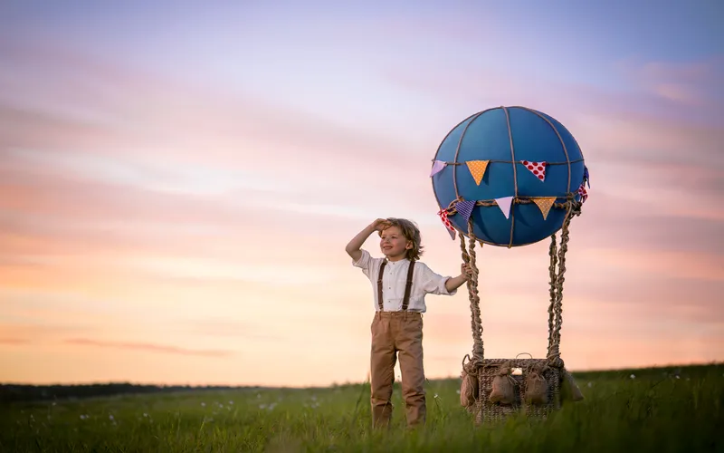 photo of a young boy standing near a small hot air balloon