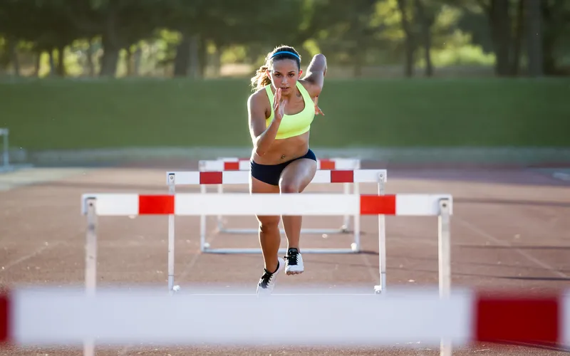 athletic woman jumping hurdles on running track