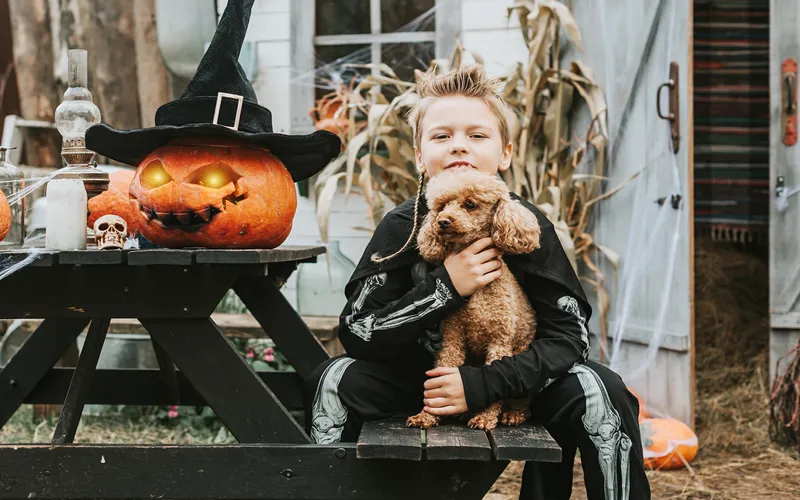 boy posing with his pet dog and a pumpkin head