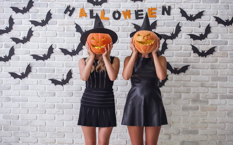 two women in goth outfits holding a pumpkin head over their faces