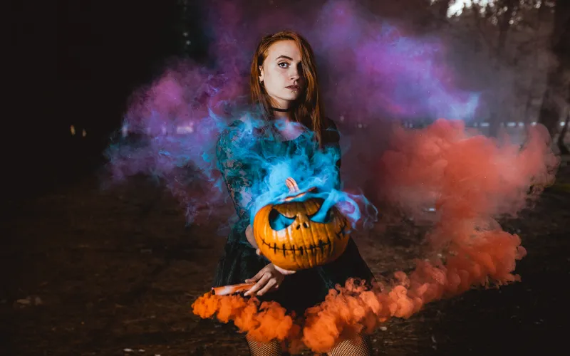 A woman posing with a Pumpkin head with smoke coming out of it -