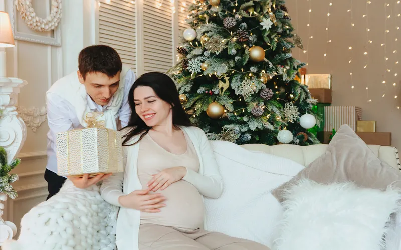 expecting couple posing next to a Christmas tree