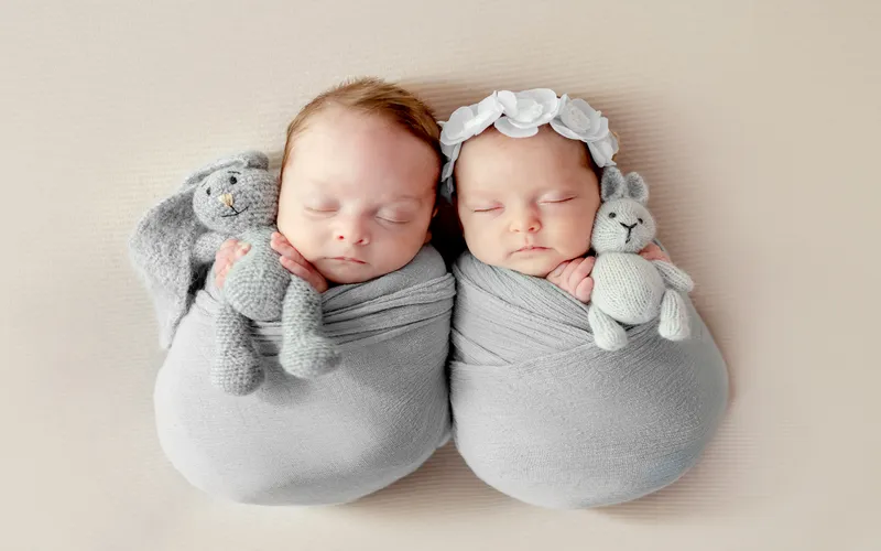 twins in matching swaddles and toys