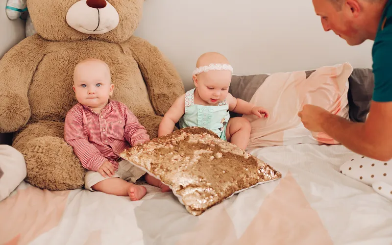 two infants sitting on bed with giant teddy bear
