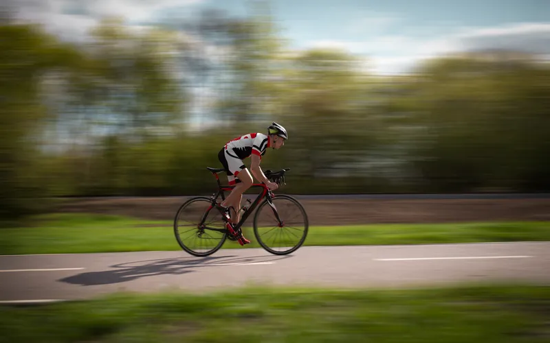 man biking on a rural road with motion blur trailing behind them at dusk