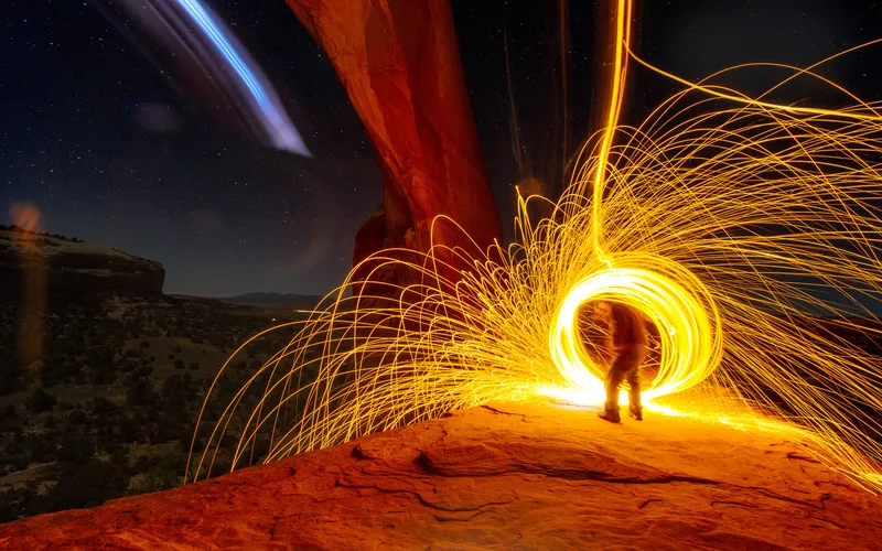 Glowing steel wool spun in circles at night creating bright orange light trail patterns