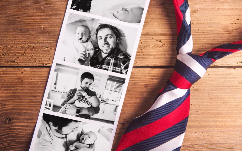 photo booth strip of father and newborn child kept on wooden table along with tie