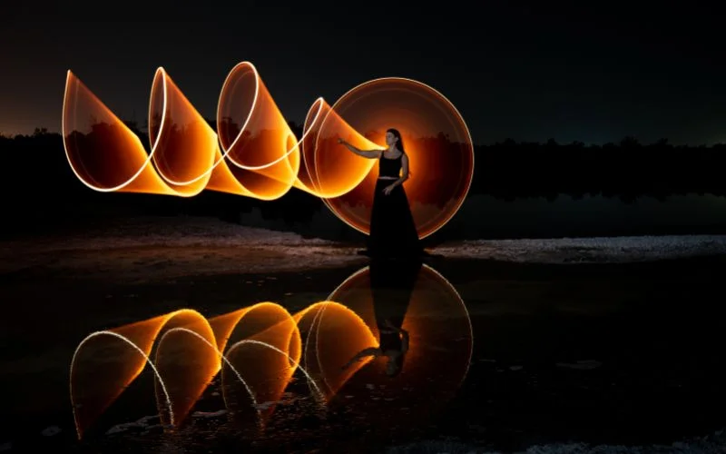 Silhouetted figure creating circular light trails at night, illustrating what aperture is best for low light photography