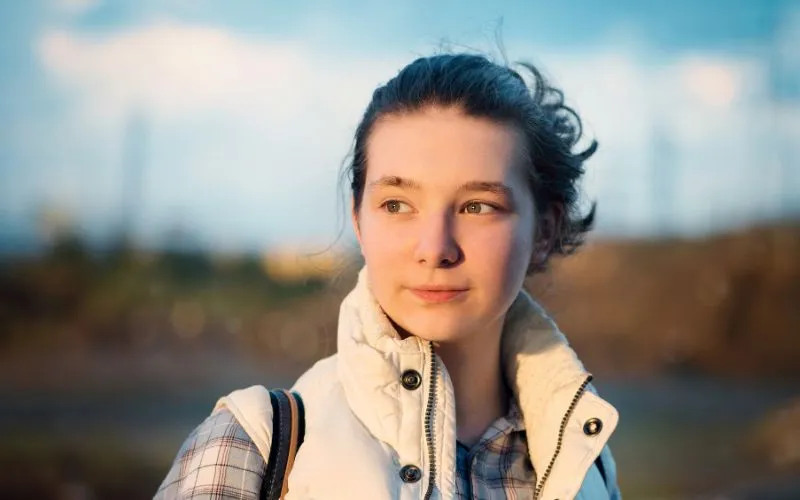 Close-up portrait of a young woman in soft warm outdoor light with a blurred background, an example for how to choose the right aperture in portraits