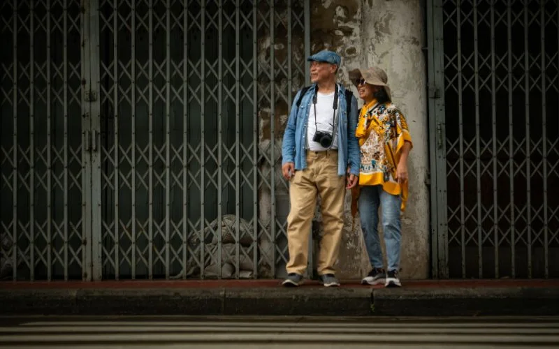 Two people walking past rows of shuttered storefronts on a city street, a street photography aperture example