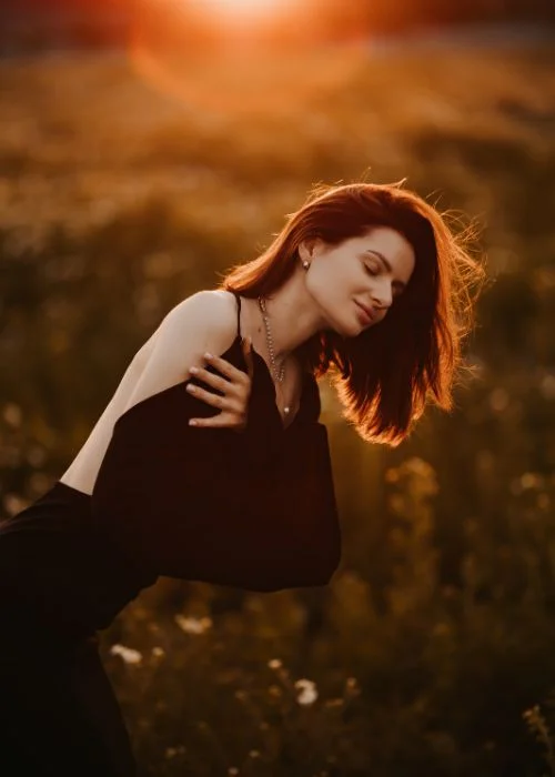 Woman with wind-blown hair backlit in a golden field, an example of golden hour photography with warm rim lighting