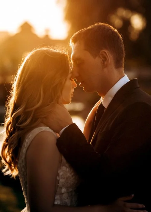 Couple embracing forehead to forehead at sunset, warm golden hour light glowing behind them