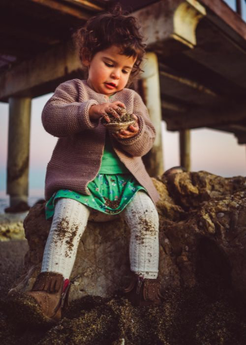 Child sitting on rocks while examining an object outdoors, capturing authentic human moments