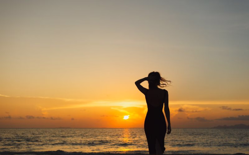 A silhouette of a woman on the beach during sunset posing for a beach photoshoot