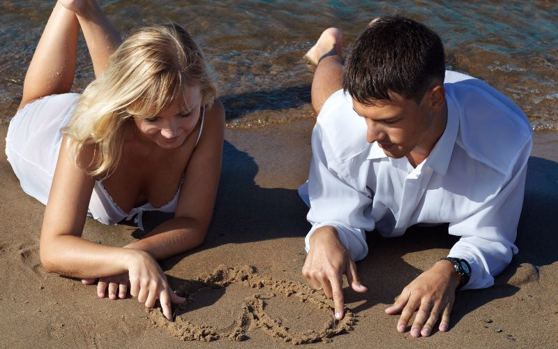 Beach photography of cute couple drawing patterns in the sand