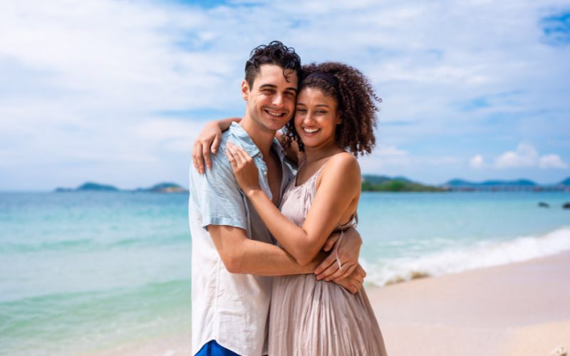 Couple poses for beach photoshoot while wrapping arms around each other