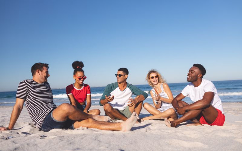 Friend group sitting in semi-circle on the beach to pose for their beach photoshoot