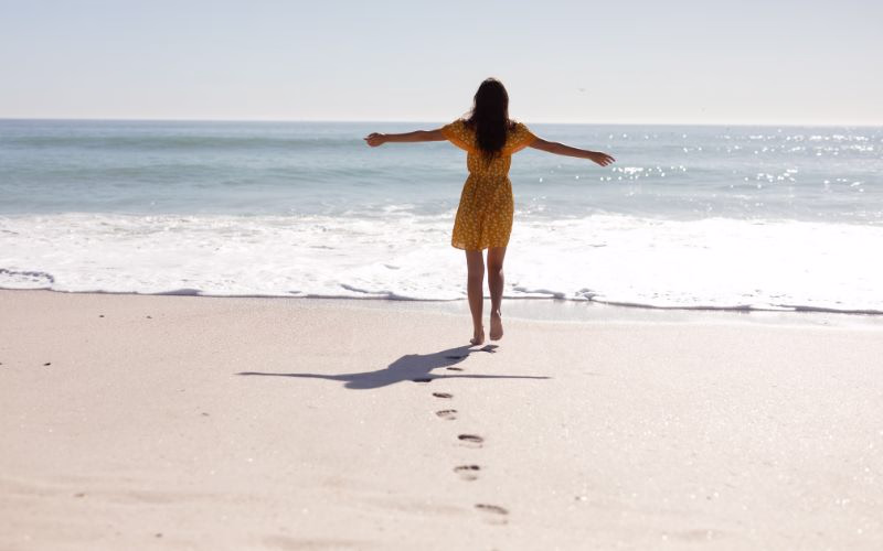 A woman walking towards the sea while leaving a trail of her footprints for beach photography