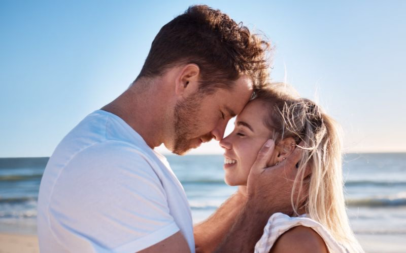 A couple poses for beach photoshoot while touching foreheads