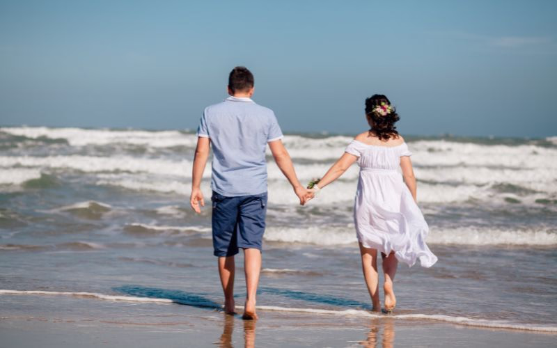 A couple poses for their beach photoshoot while walking on the shoreline holding hands