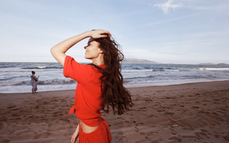 A photo of a woman caressing her hairs on the beach as wind flows