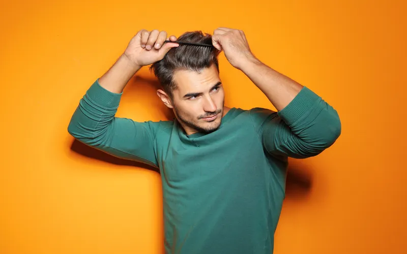 Handsome man styling hair on orange background