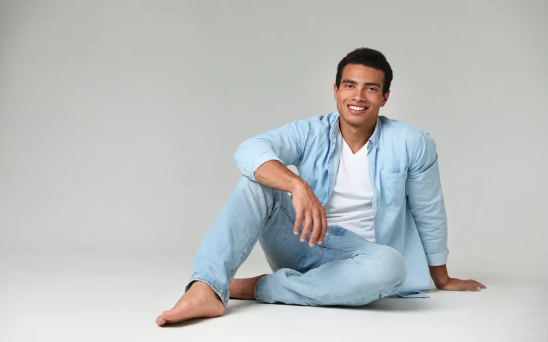 Man in denims casually sitting relaxed on white floor