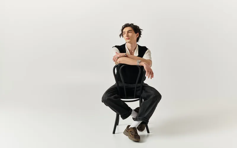 stylish man posing for photo while sitting on chair backwards